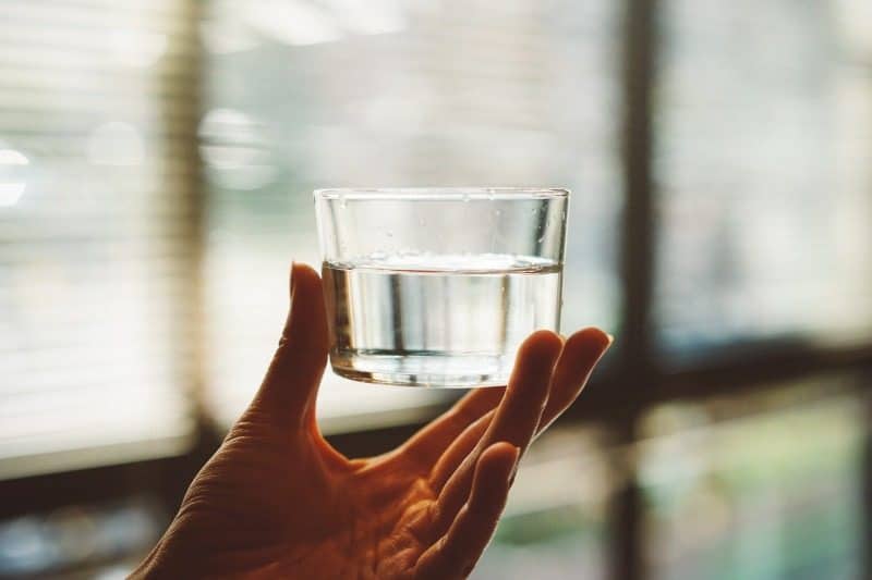 A hand holds a glass of crystal-clear water, representing the transparency retrospective meetings promote