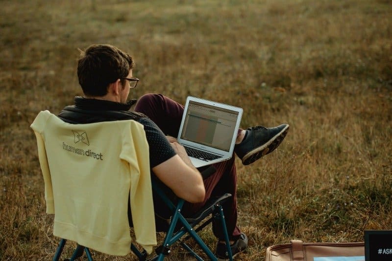 Persona trabajando de forma remota con su laptop al aire libre, sentada en una silla plegable